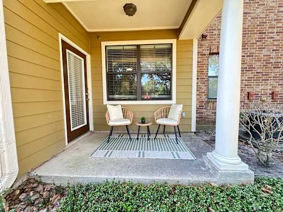 A small porch with a grey rug and two chairs.