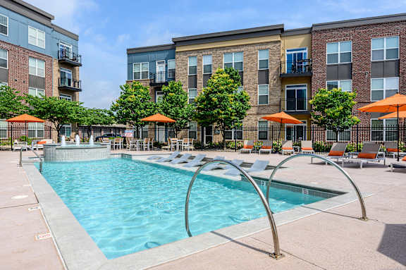 A swimming pool surrounded by orange umbrellas and lounge chairs. at Penn Circle, Carmel, IN, 46032