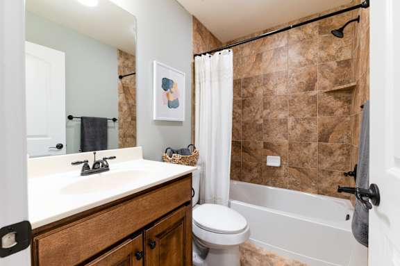 A bathroom with a brown tiled shower area and a white toilet.