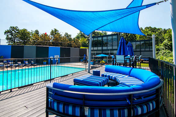 A blue and white striped sun lounger sits on a wooden deck next to a pool.