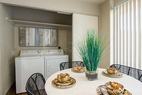 A dining table set with plates and a vase of grass in the middle.