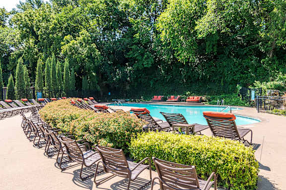 A pool surrounded by trees and chairs.