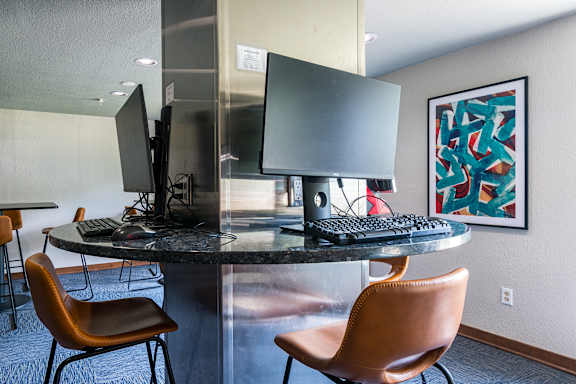 A modern workspace with a round table, two chairs, and a computer setup.