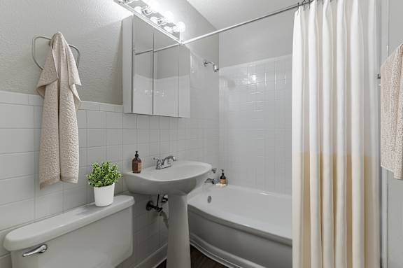 A white bathroom with a white sink, white tub, and white shower curtain.