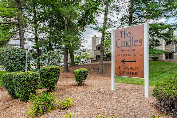 A sign for The Candles Apartments leasing center is in front of a building and trees.
