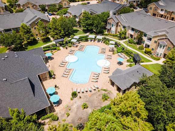 A bird's eye view of a residential area with a swimming pool surrounded by houses and trees at Waterstone at Cinco Ranch Apartments, Texas