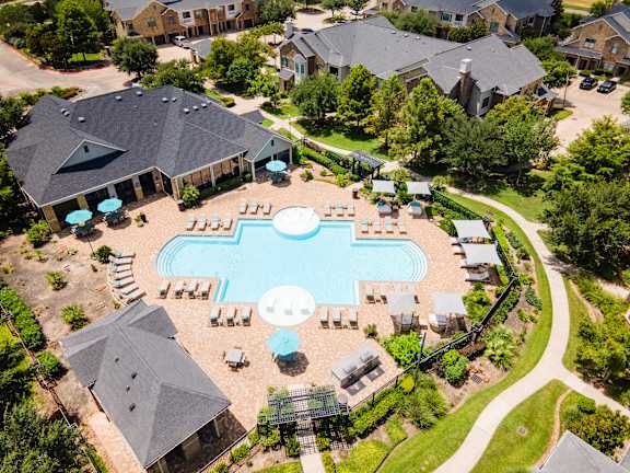 An aerial view of a swimming pool surrounded by houses and trees at Waterstone at Cinco Ranch Apartments, Texas, 77450
