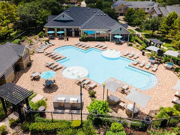 A large swimming pool surrounded by lounge chairs and umbrellas at Waterstone at Cinco Ranch Apartments, Katy, TX