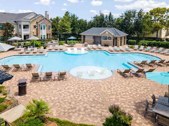 A large outdoor swimming pool surrounded by lounge chairs and umbrellas at Waterstone at Cinco Ranch Apartments, Katy, 77450