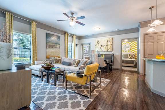 A living room with a yellow chair and a grey and white patterned rug at Waterstone at Cinco Ranch Apartments, Texas, 77450
