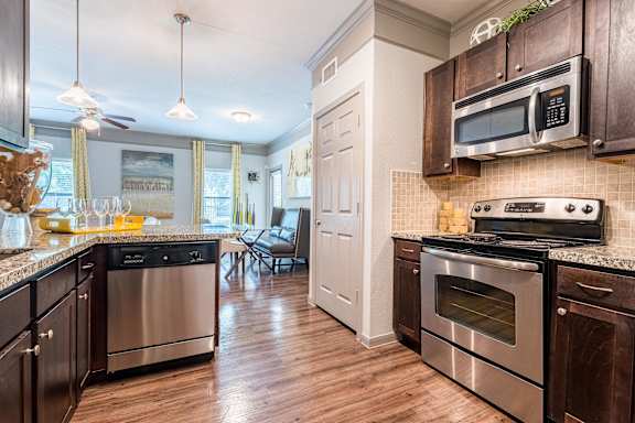 A kitchen with dark wood cabinets and stainless steel appliances at Waterstone at Cinco Ranch Apartments, Katy Texas