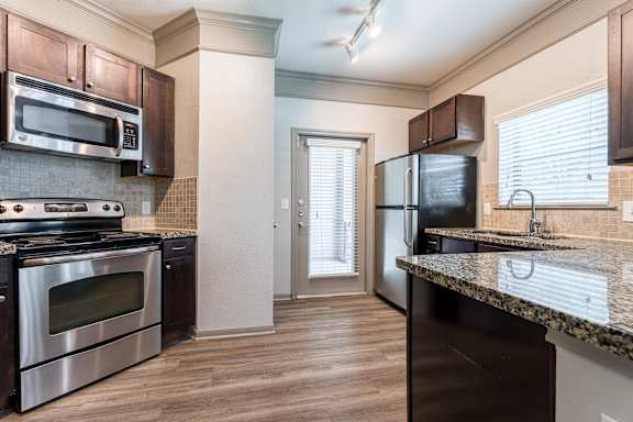 A kitchen with dark brown cabinets and stainless steel appliances at Waterstone at Cinco Ranch Apartments, Texas, 77450