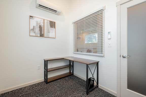 A room with a window, a bench, and a painting on the wall.