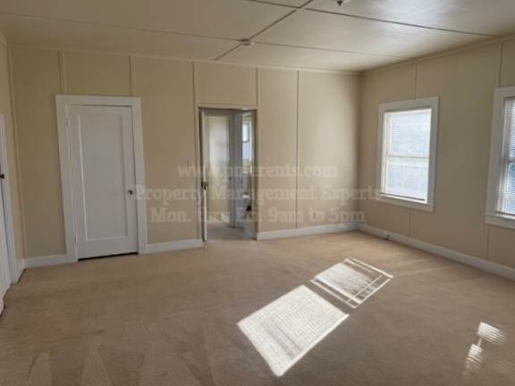 A room with a carpet, a door, a window, and a wall with a window.