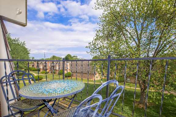 A balcony with a table and chairs overlooking a green lawn.