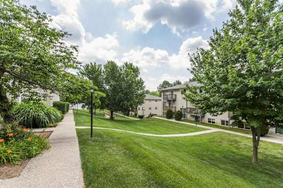 A pathway leads through a grassy area with trees and a building in the background.