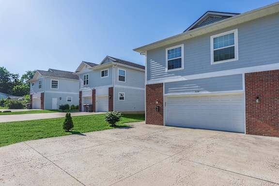 A house with a grey garage door and a small tree in front.