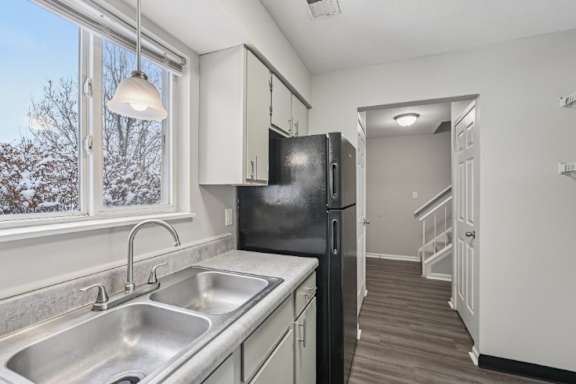 A kitchen with a black refrigerator and a stainless steel sink.