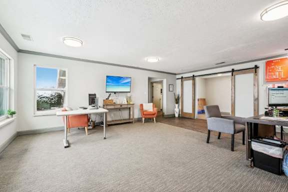 A room with a desk, chairs, and a TV on the wall.