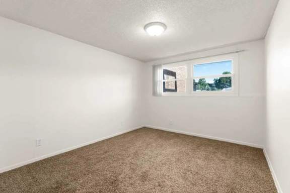 A room with a carpeted floor and a window showing a building and trees outside.