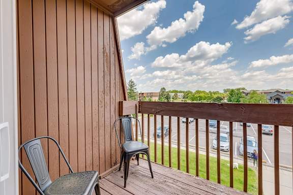 A chair sits on a wooden deck with a view of a parking lot and trees.