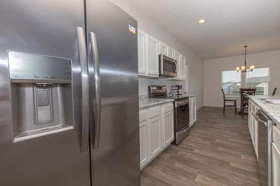 A modern kitchen with a stainless steel refrigerator and wooden flooring.