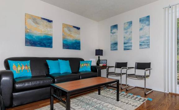 A living room with a black couch and a painting on the wall.