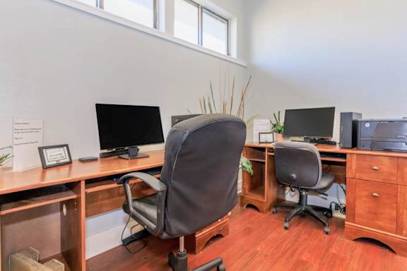 A room with a desk, chairs, and computers.