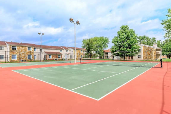 A tennis court is surrounded by apartment buildings.
