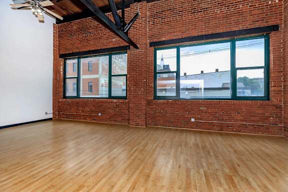 A room with wooden floors and a brick wall with windows.
