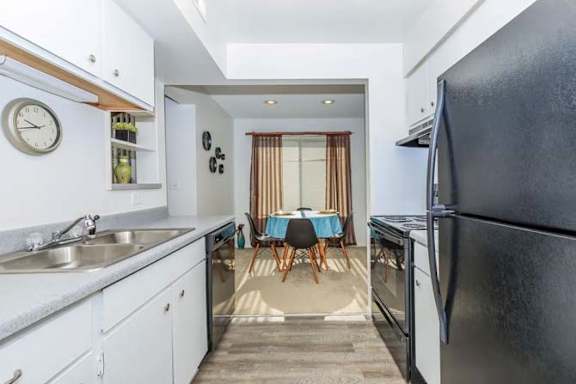 A kitchen with a black refrigerator and a dining table with chairs.