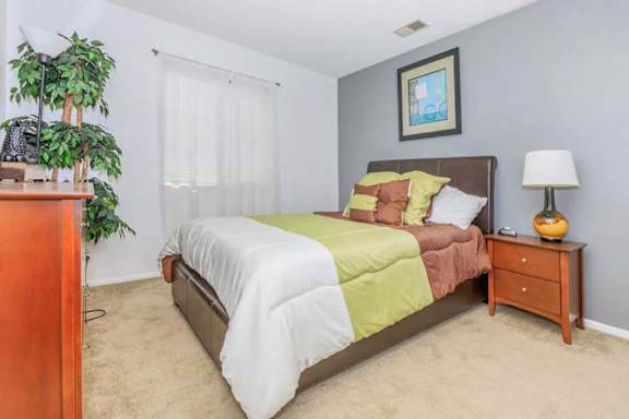 A bedroom with a bed, nightstand, and a potted plant.