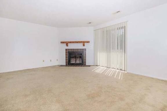 A large empty room with a fireplace and carpeted floor.