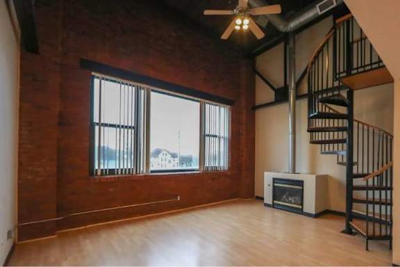 A room with a wood floor, a staircase, and a fireplace.
