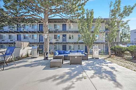 a patio with furniture and trees in front of a building at Park at Fitzsimons Apartments, Colorado