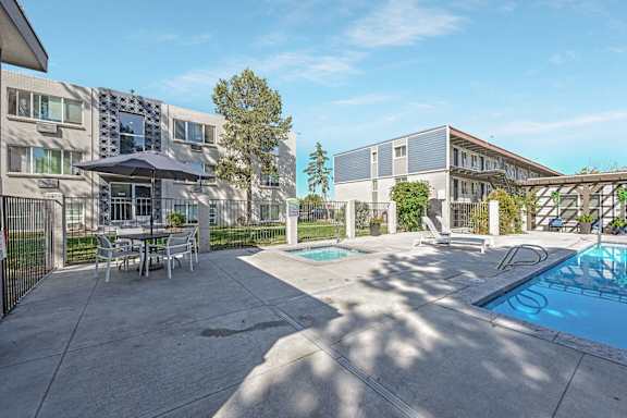 A poolside area with a table and chairs and a building in the background at Park at Fitzsimons Apartments, Aurora