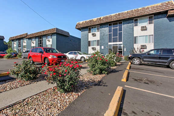 A parking lot with a red car and a building in the background.