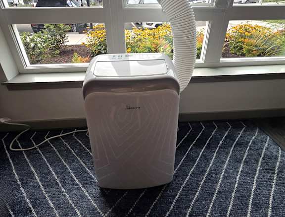 A white vacuum cleaner is on a striped carpet by a window.