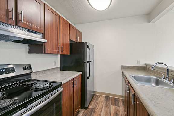 A kitchen with a black stove top oven, black refrigerator, and wooden cabinets. at Brookstone, SeaTac, Washington