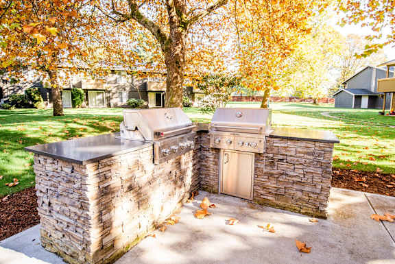 A stone outdoor kitchen with a grill and sink at Bellamy Park Apartments , Lakewood, 98498