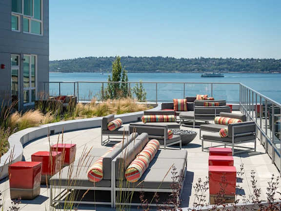 A patio with red and grey furniture overlooks a body of water.