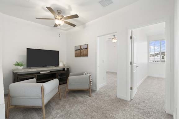 A living room with a television, two chairs, and a ceiling fan.