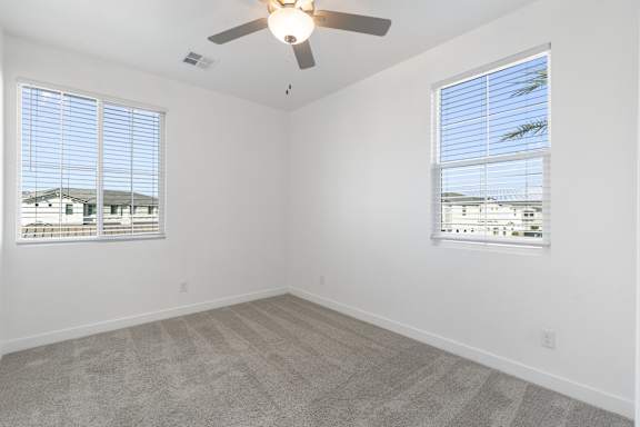 A room with a ceiling fan and two windows.