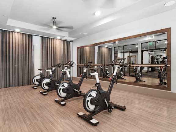 A gym with a row of stationary bikes and a mirror reflecting the room.