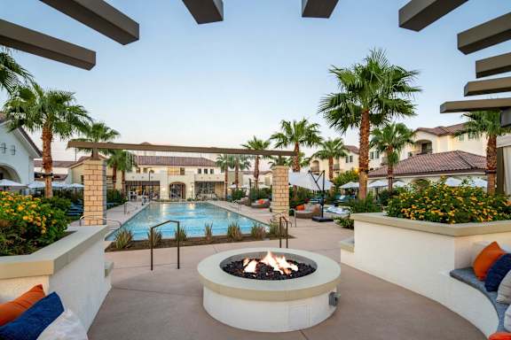 A patio with a fire pit and a pool in the background.