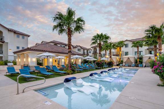 A pool surrounded by palm trees and lounge chairs.