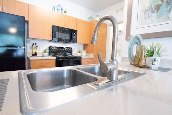 A kitchen with a black refrigerator and a stainless steel sink.