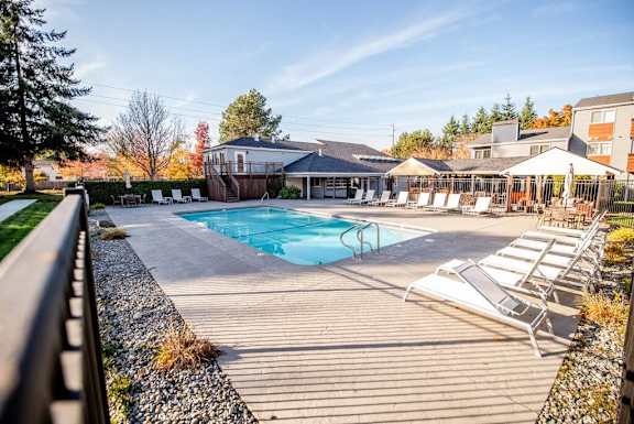A pool area with sun loungers and a building in the background. at Northpoint Apartments, Washington, 98407