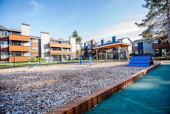 A playground with a blue slide and a pebble-covered area in front of apartment buildings. at Northpoint Apartments, Tacoma, WA