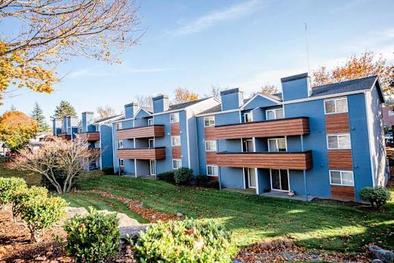 Apartment complex with blue and brown buildings surrounded by trees and grassy areas. at Northpoint Apartments, Tacoma, WA